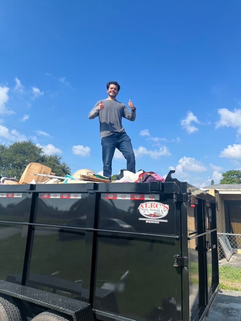 Worker standing on top of a fully loaded junk removal trailer after an eviction cleanout with two full loads in Opa-Locka.